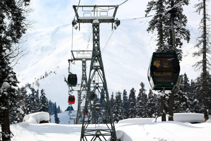 Skiers and tourists ride in a gondola lift, passing over the snow-covered slopes of the famous Gulmarg ski resort in Baramulla district, Jammu and Kashmir, India, on February 12, 2023. The gondola lift offers views of the Himalayan mountains and provides access to higher reaches for winter sports enthusiasts. (Photo by Nasir Kachroo/NurPhoto via Getty Images)